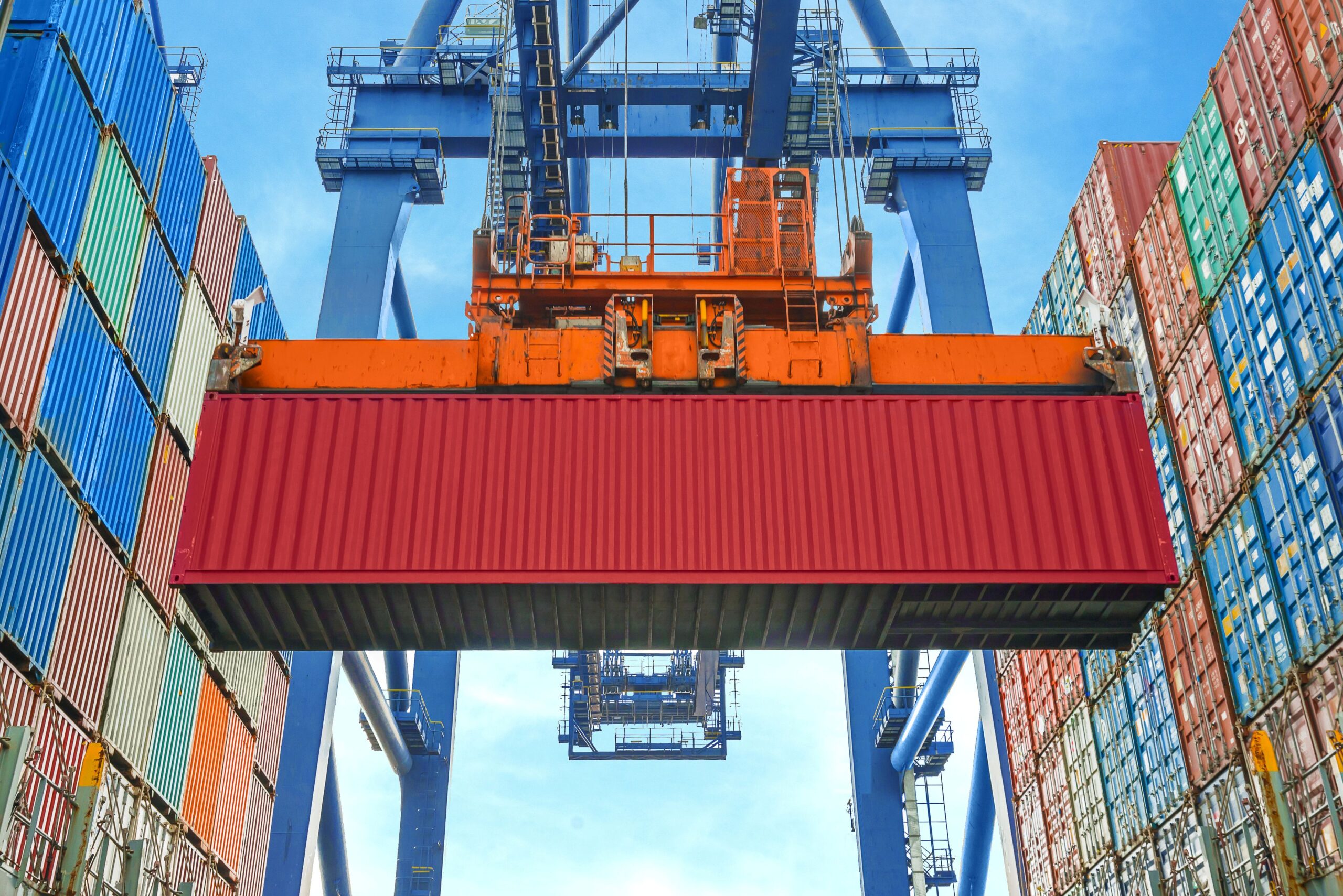 Containerkran hebt roten Container zwischen gestapelten Einheiten – Symbol für modulare Verladetechnik und Digitalisierung Hafen